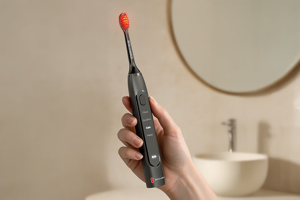 Person holding a black electric toothbrush with red bristles in a bathroom setting.