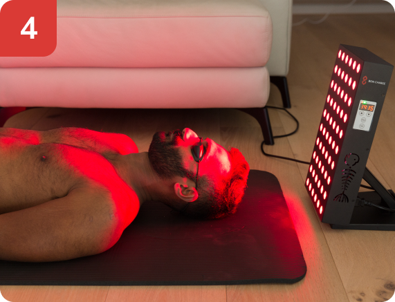 man laying on mat in front of a small red light device